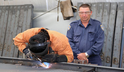 An Overseer monitoring an inmate drilling metal object