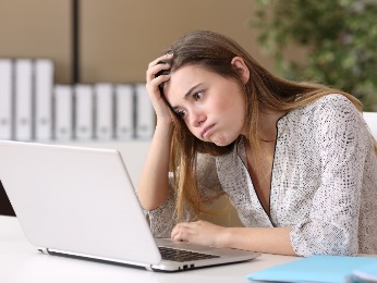 A woman with her head in her hand, trying to work on her laptop. 