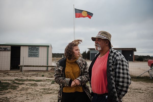 A man and girl standing in front of an Aboriginal flag