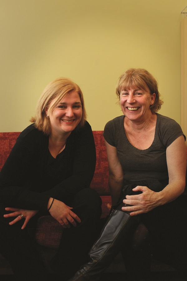 Two adult females sitting next to each other smiling at the camera