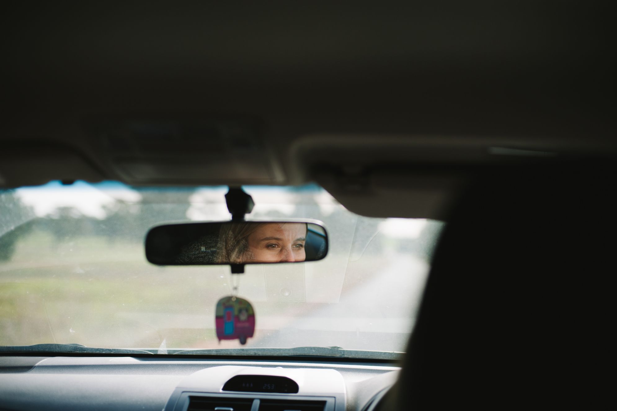 A picture of a female looking through a rear view mirror in a car