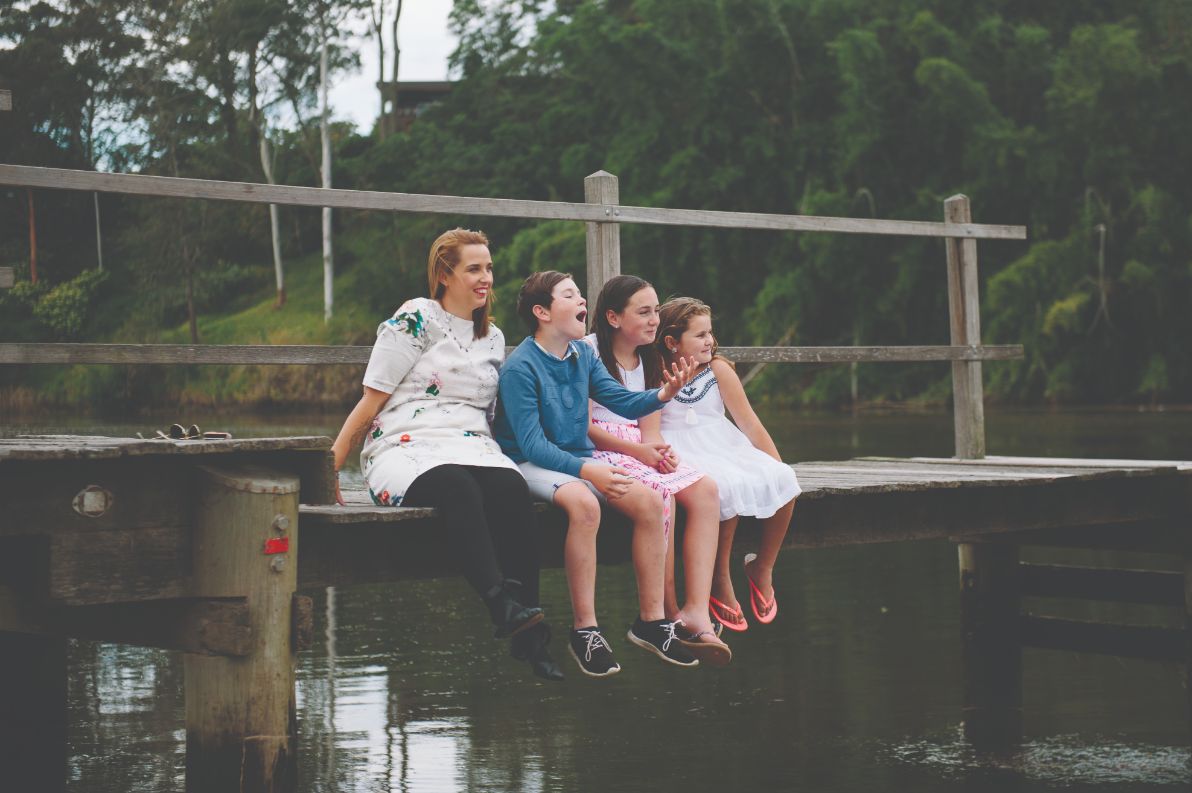 A female with three children sitting next to a river on a wooden jetty