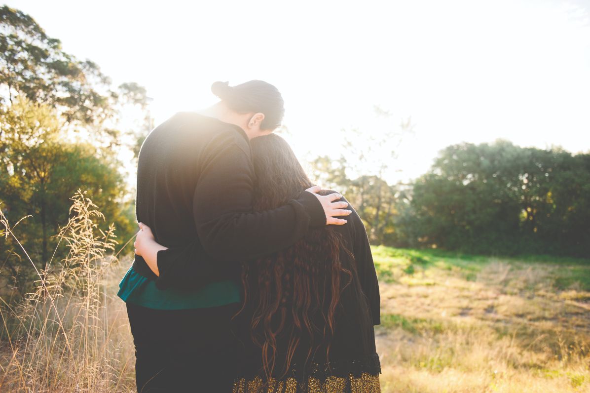 A man and women with their back to the camera hugging as the sun is rising or setting in the distance
