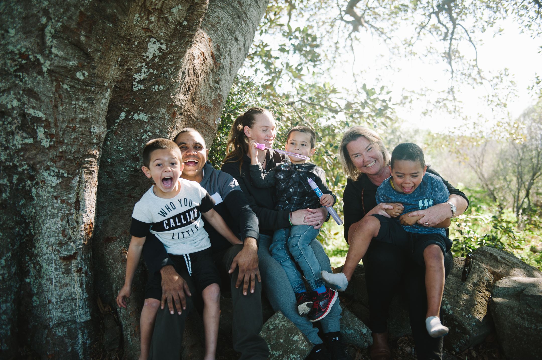 Sheri and her husband Bundy, along with case worker Amber, sitting under a tree, each holding one of three boys