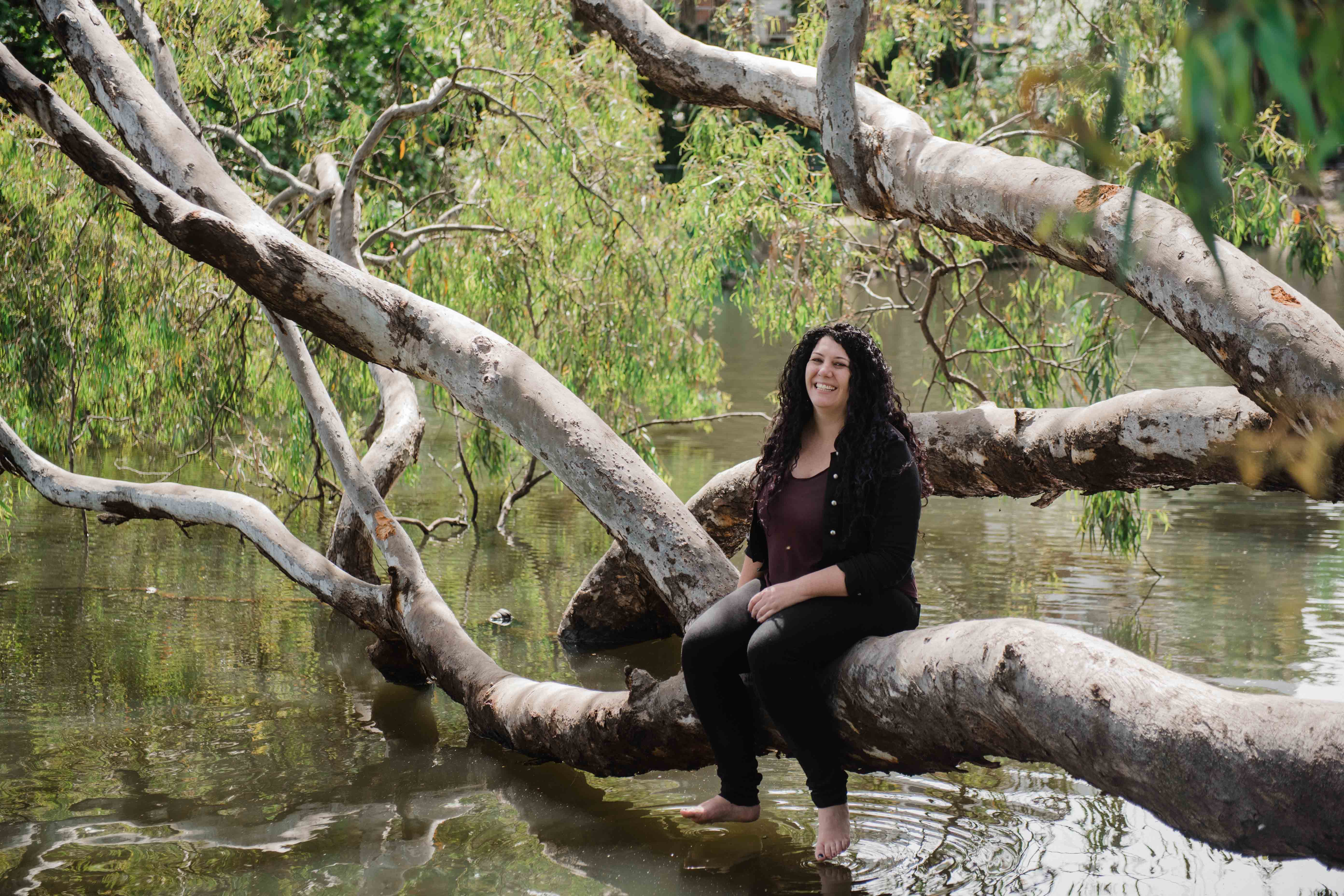 Jade sitting on a fallen tree in the river smiling 