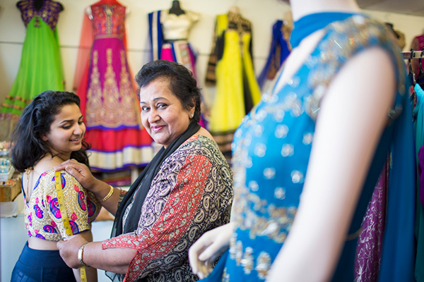 Yasmin measuring a blouse for a young woman, surrounded by colourful traditional women's clothing in a shop.