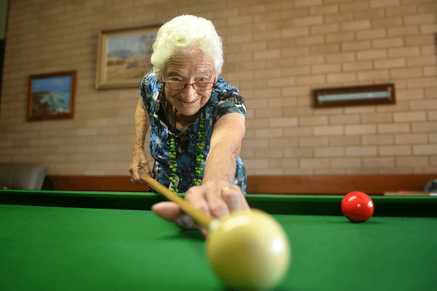 Betty leaning over a billiard table, positioning the cue to hit a ball.