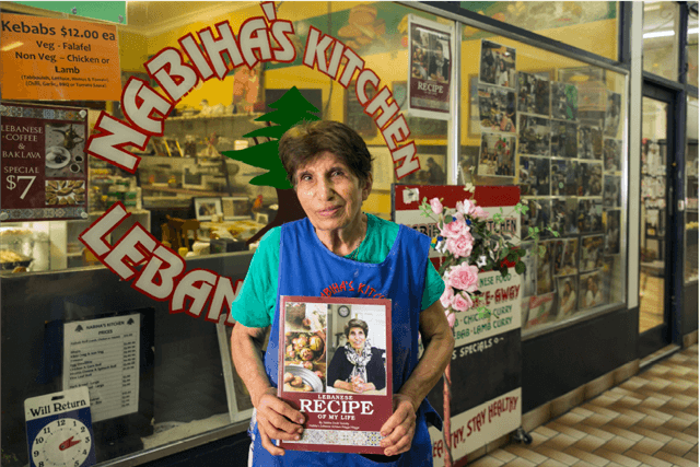 Nabiha holding recipe book in front of a lebanese kitchen shop