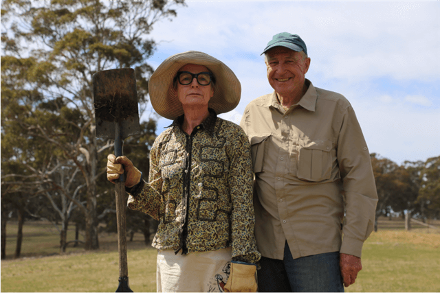Pauline holding shovel and David standing next to Pauline in an open field