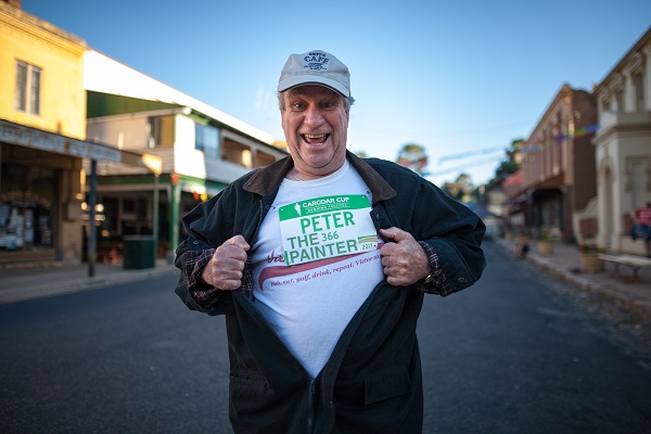 Peter Griffin standing in the street, holding apart his shirt to show another shirt underneath with a Carcoar Cup sign pinned to it saying Peter the Painter, 366.