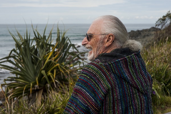 Phil Burton sitting outside surrounded by grasses, looking out at the ocean.