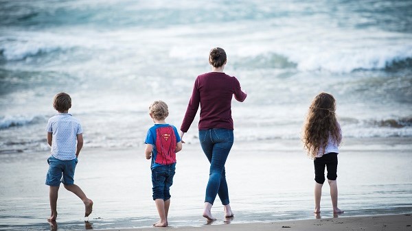 Ella walking with her three children towards the water at the beach. Their back is towards the camera. 