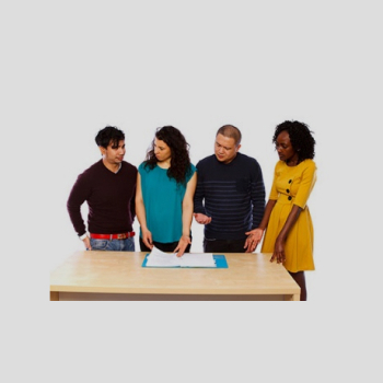 A group of people talking while standing around a table.