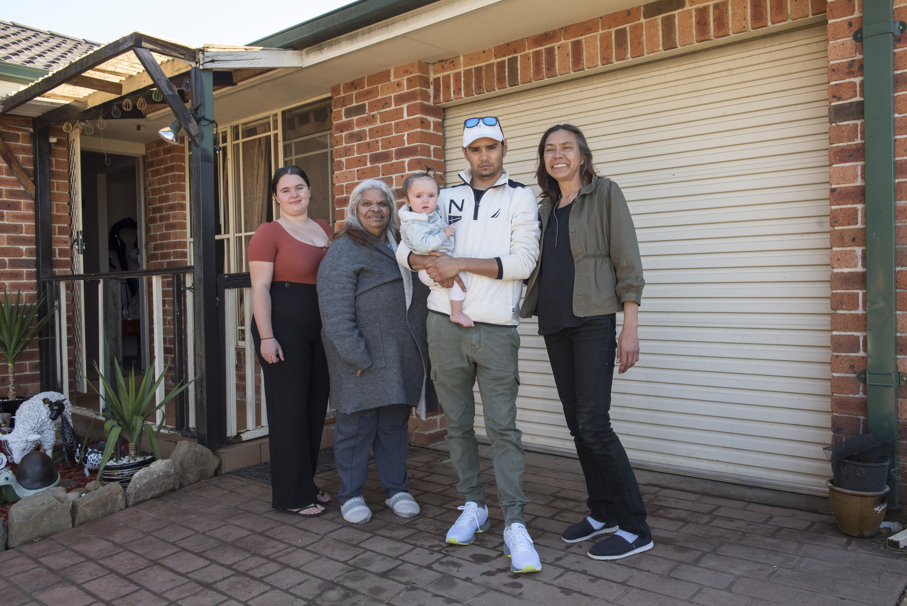 An Aboriginal family holding a baby stand in front of their house